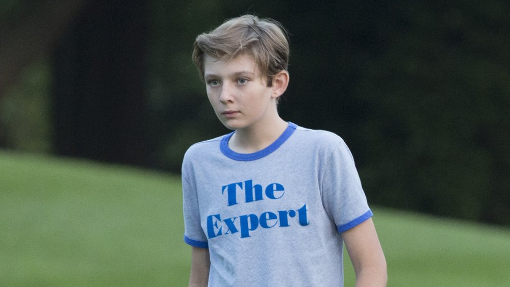 Barron Trump walking outside in a blue t-shirt