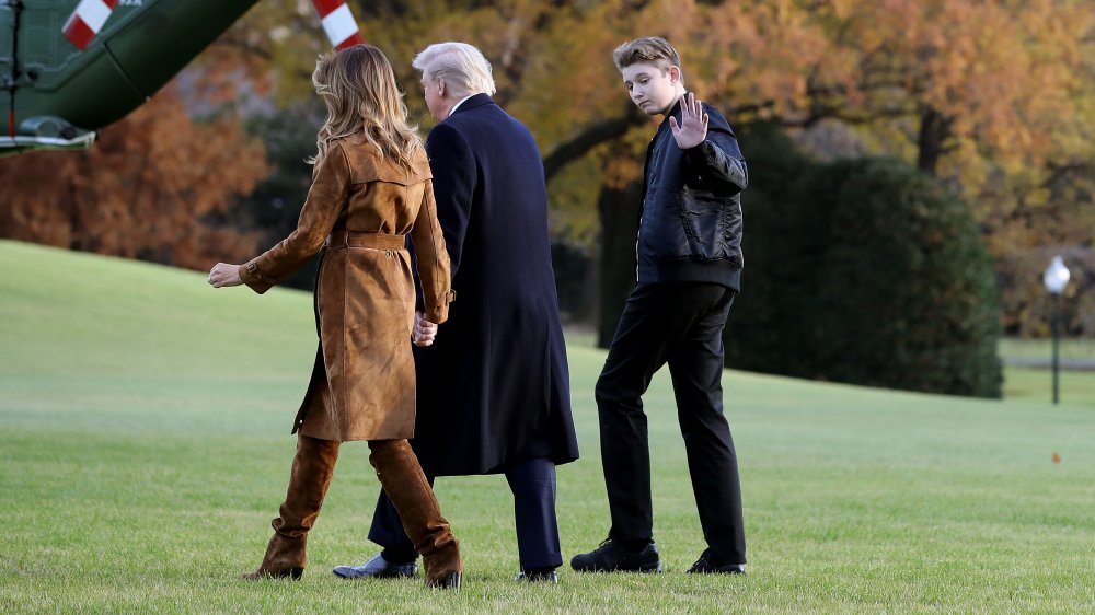 Barron Trump in all black, waving while walking alongside Melania and Donald Trump