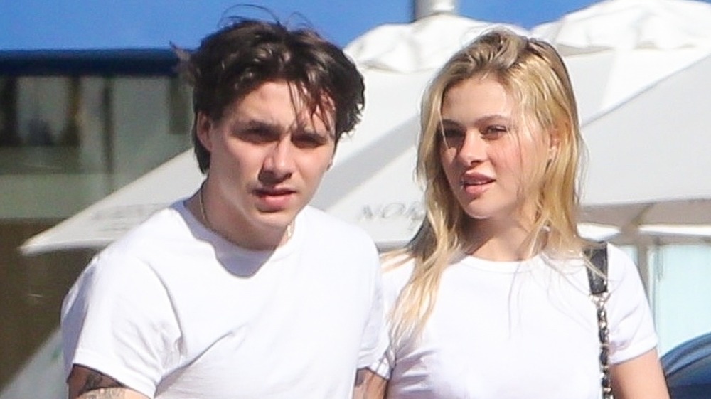 Brooklyn Beckham and Nicola Peltz wearing matching white t-shirts, walking outside 