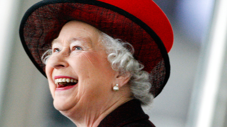 Queen Elizabeth laughing in red and black hat and outfit 