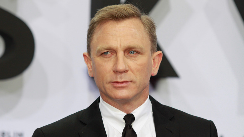 Daniel Craig with a serious expression wearing a suit on the red carpet