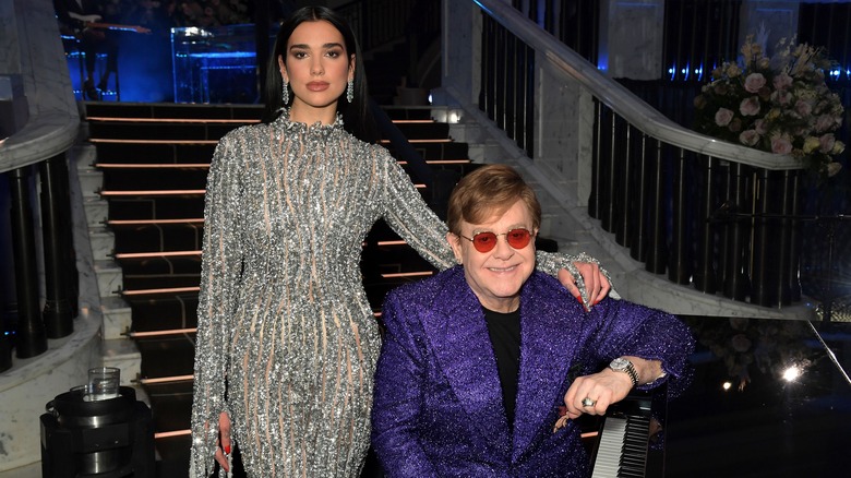 Dua Lipa posing next to Elton John, seated