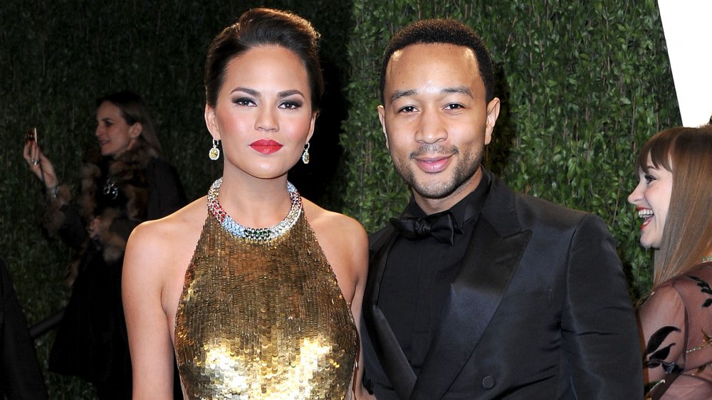 Chrissy Teigen in a gold gown standing with John Legend