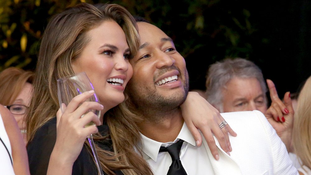 Chrissy Teigen holding a champagne glass, hugging John Legend