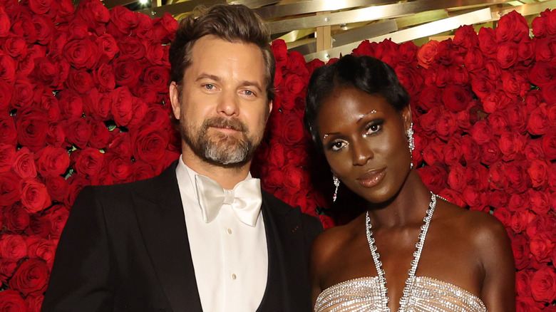 Joshua Jackson and Jodie Turner-Smith smiling together in front of red floral arrangement