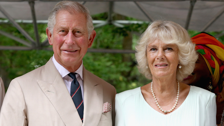 King Charles and Queen Camilla, smiling together in the shade