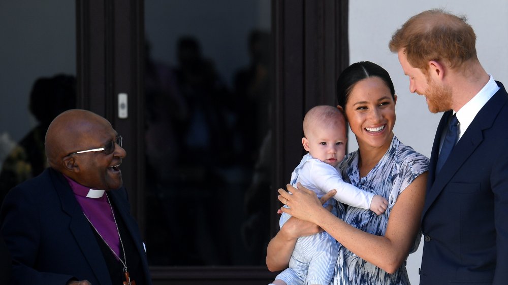 Desmond Tutu looking at Baby Archie in Meghan Markle's arms next to Prince Harry