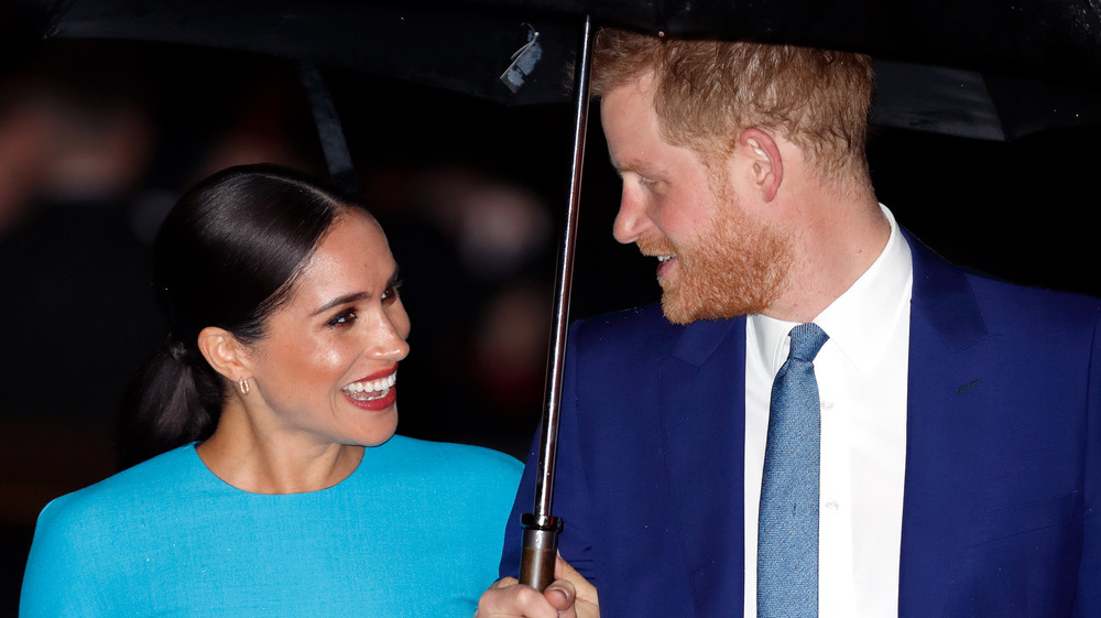 Meghan Markle and Prince Harry smile at each other under an umbrella