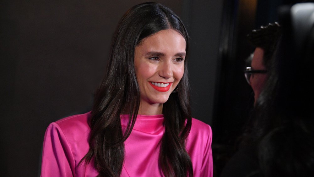 Nina Dobrev in a bright pink dress, smiling during a conversation