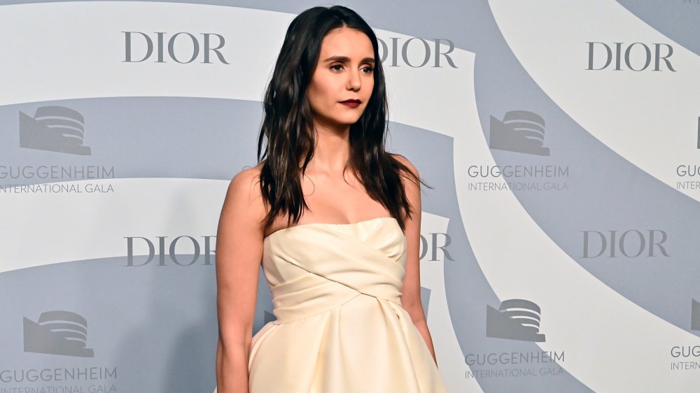 Nina Dobrev in a strapless cream dress, posing at an angle with a serious expression