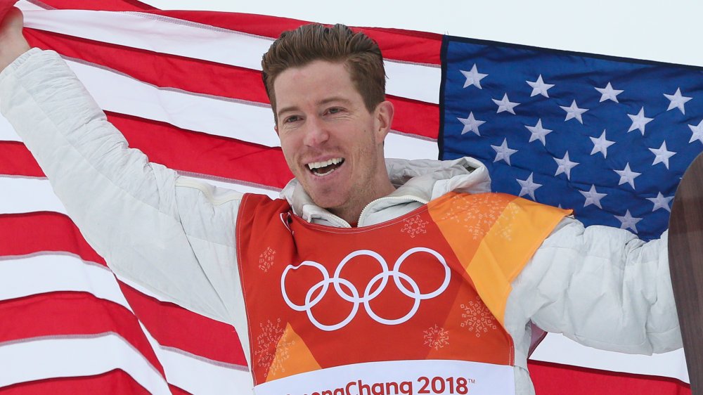 Shaun White smiling and holding the American flag at the 2018 Winter Olympics