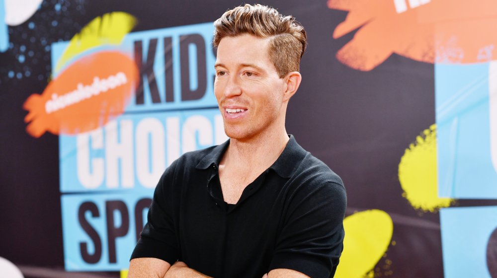 Shaun White in a black polo t-shirt, smiling and posing with his arms crossed at the 2019 Kids Choice Awards