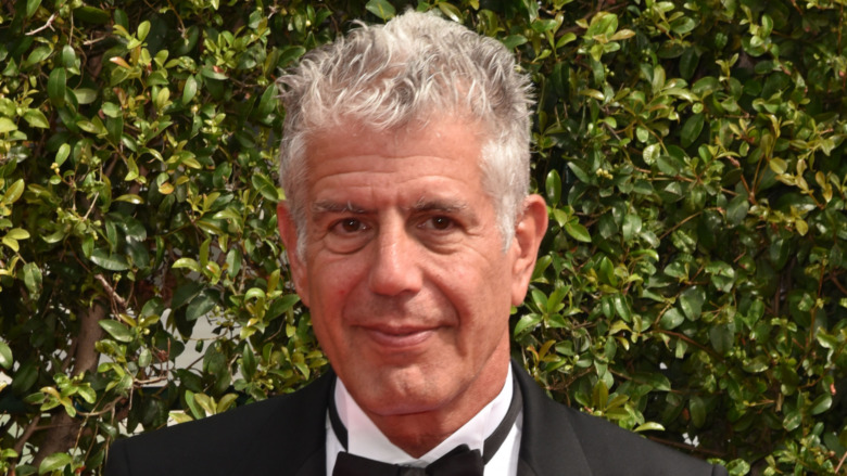 Anthony Bourdain in a suit on the red carpet in front of a bush