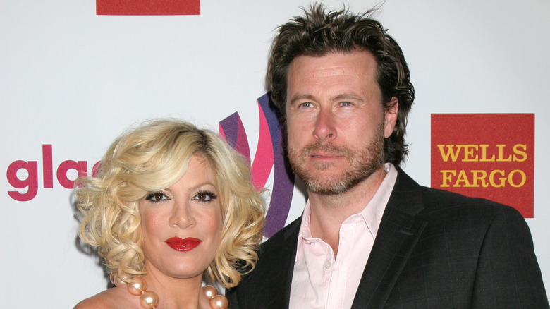 Tori Spelling and Dean McDermott pose together in front of a step and repeat