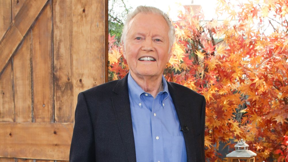 Jon Voight smiling in front of autumn leaves