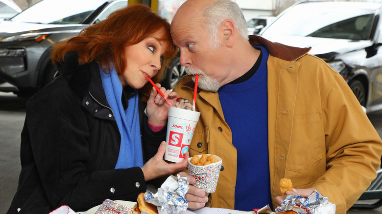 Reba McEntire and Rex Linn looking into each other's eyes sipping milkshake