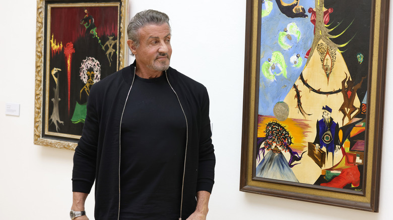 Sylester Stallone standing next to paintings