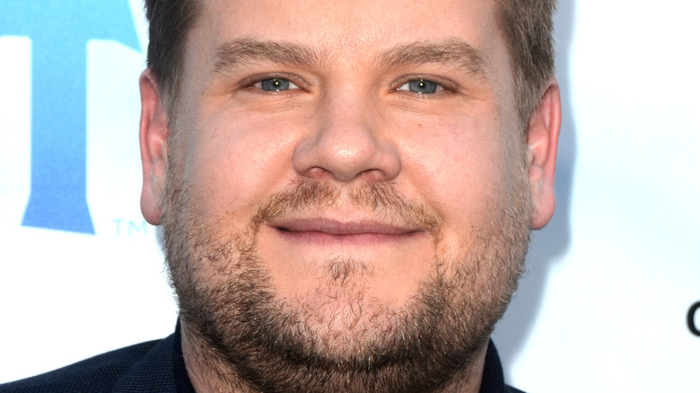 James Corden wears a black shirt and blue blazer