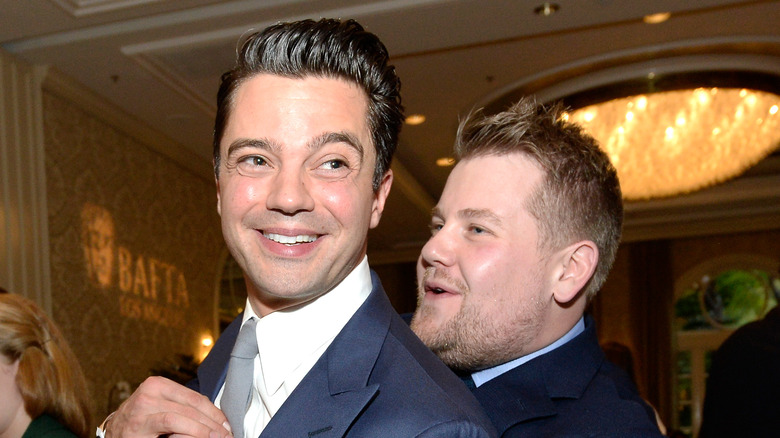 Dominic Cooper and James Corden pose at an even as Corden hugs Cooper and the two smile