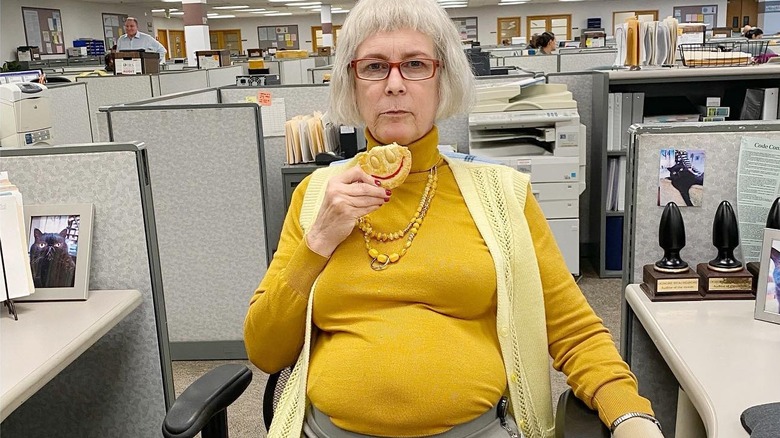 Jamie Lee Curtis sitting in an office chair eating a cookie
