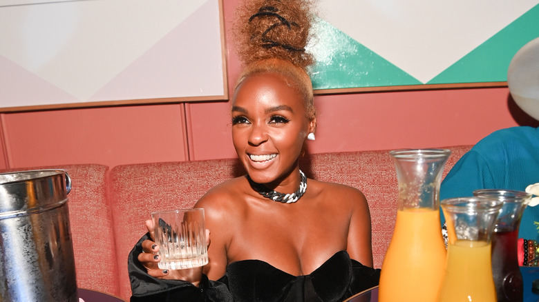 Janelle Monae sitting, holding a glass