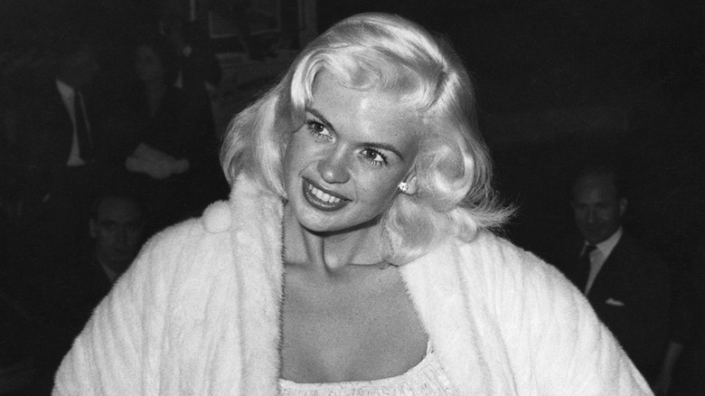 Jayne Mansfield posing in a white coat at an event in the 50s.