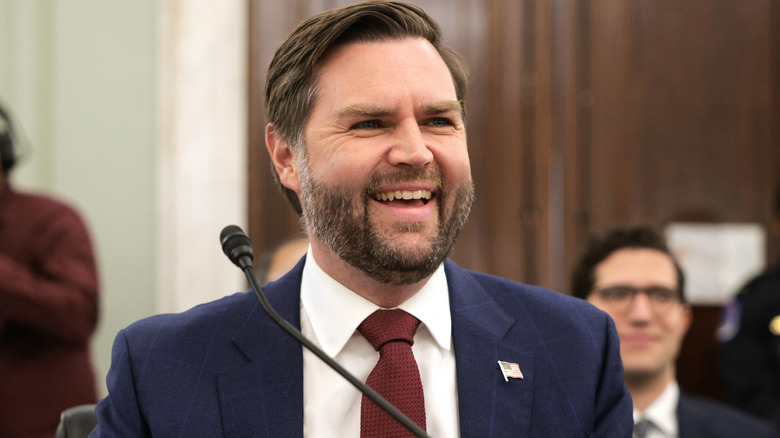 JD Vance grinning behind a microphone