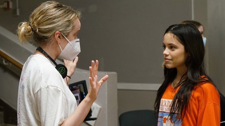 Director Megan Park in a white shirt and face mask with Jenna Ortega in an orange t-shirt with long dark hair