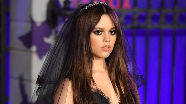 Jenna Ortega wearing a black veil and tiara and a black lace gown with long straight brown hair