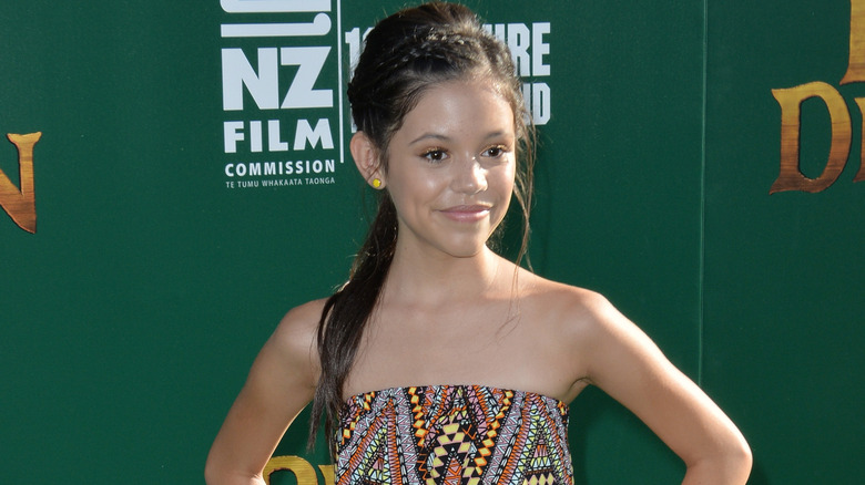 Jenna Ortega wearing a patterned strapless sundress with yellow earings and braided brown hair