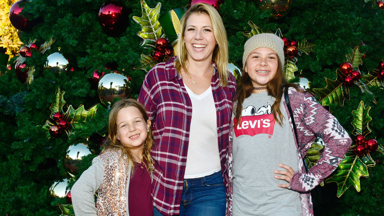 Jodie Sweetin smiling with daughters Beatrix and Zoie in from of a Christmas tree