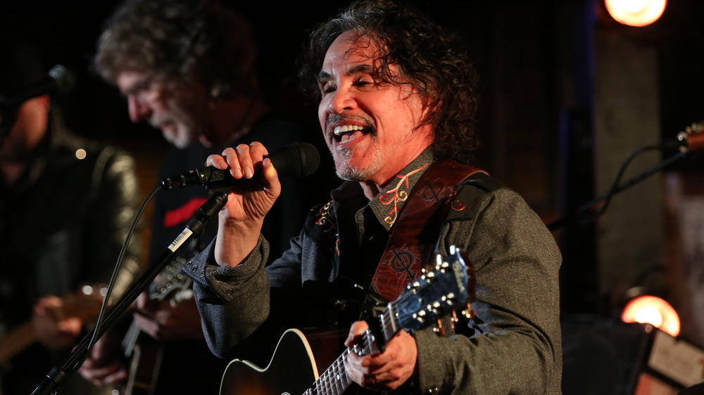 John Oates of Hall & Oates smiling and singing into a microphone 