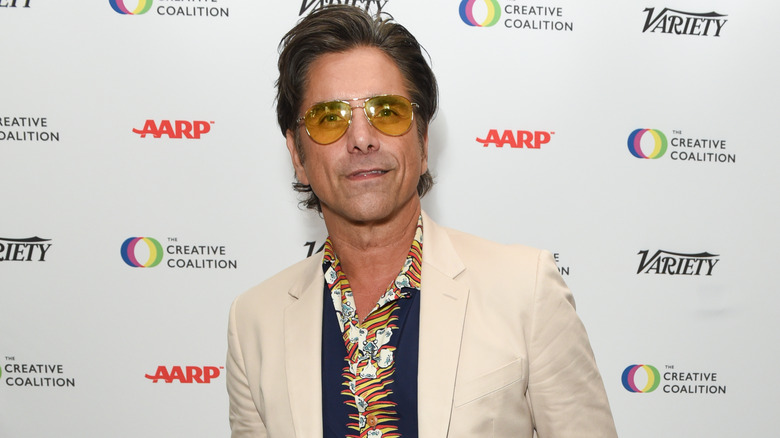 John Stamos wearing aviator sunglasses and tan jacket