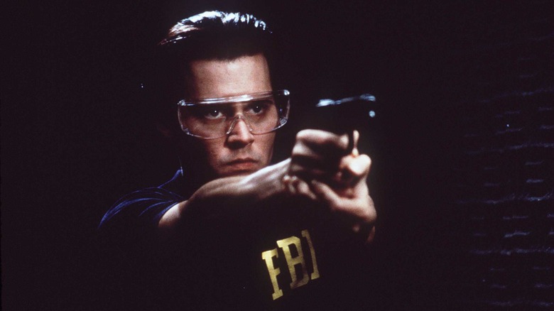 Johnny Depp wearing protective glasses and an FBI vest while shooting a gun