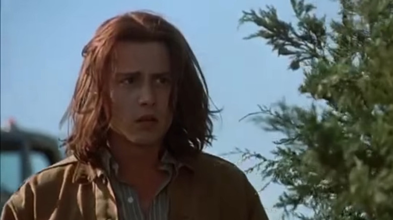 Johnny Depp with long hair wearing a brown jacket and striped button-down shirt