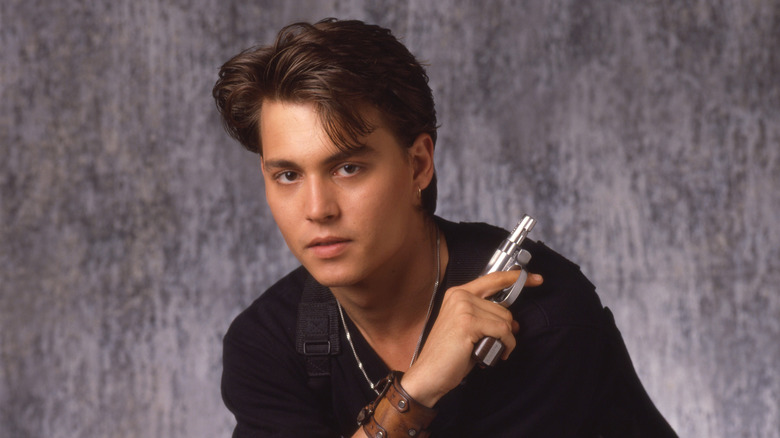 Johnny Depp wearing a black shirt, silver chain, and holding a small pistol