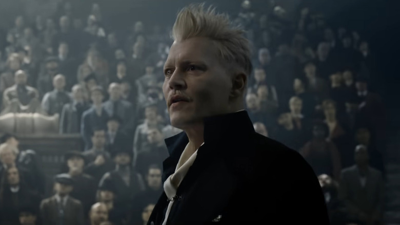 Johnny Depp in costume wearing a black high collared jacket, white shirt and tie, and blonde spiky hair