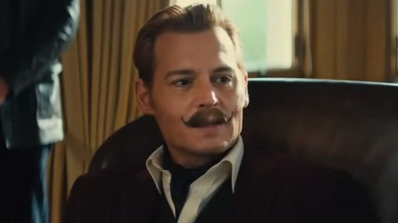 Johnny Depp wearing a black jacket, white collared shirt, and a twirled mustache