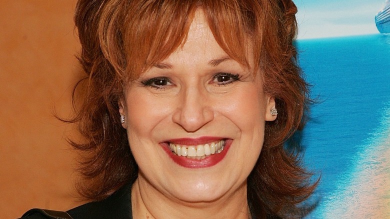 Joy Behar smiling widely against a cruise ad