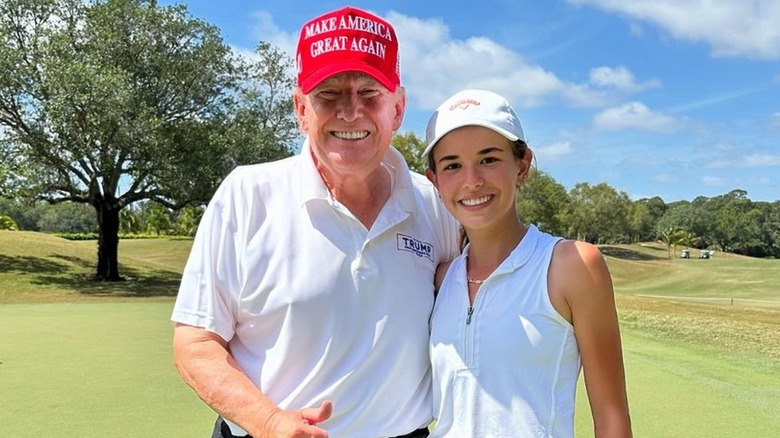 Donald Trump smiling on a golf course with Kai Trump