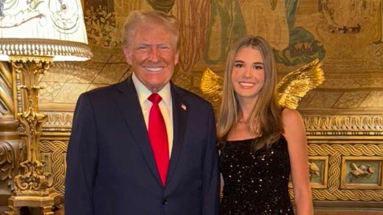 Donald Trump posing with granddaughter Kai Trump in front of gold gecor