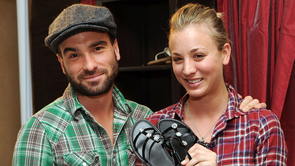 Kaley Cuoco holding up shoes beside Johnny Galecki