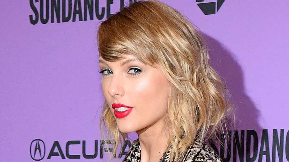 Taylor Swift smiling and looking sideways, wearing bright red lipstick