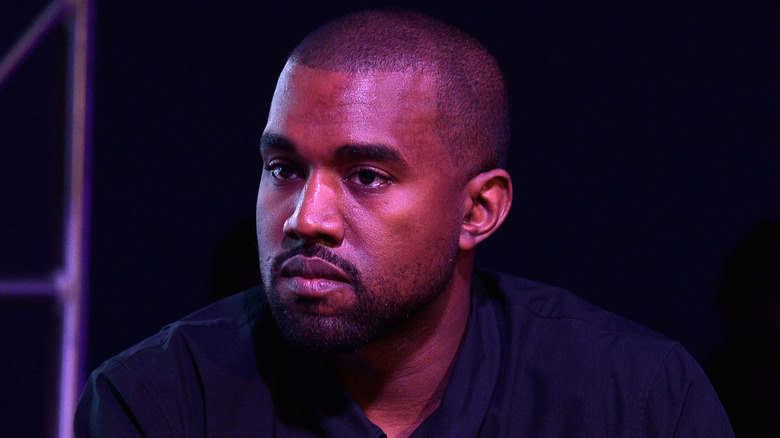 Kanye Ye West grimaces on stage in front of purple  lights