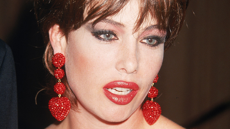 Kelly LeBrock wears red lipstick and matching drop earrings.