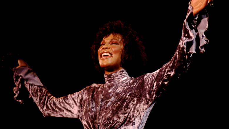 Whitney Houston singing on stage with arms up