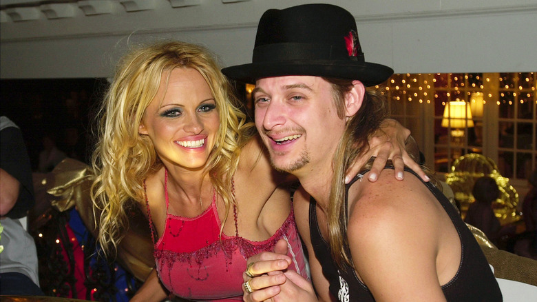 Kid Rock and Pamela Anderson laugh sitting at a table in 2001