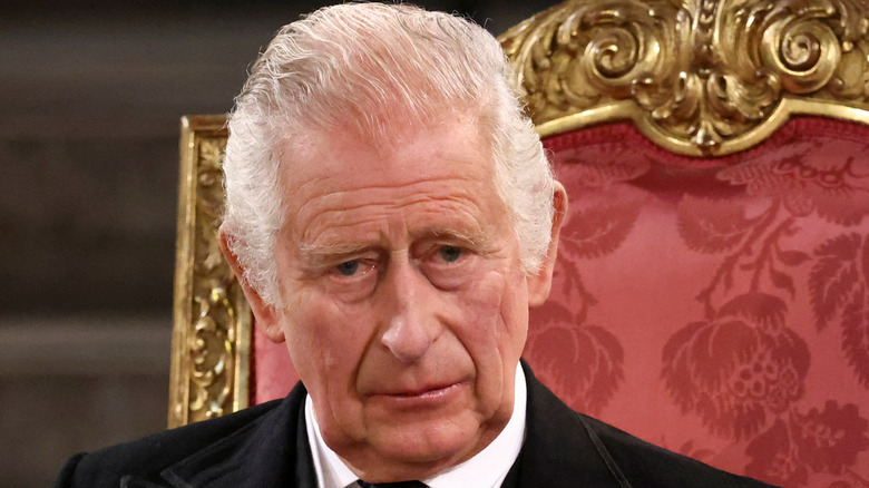 King Charles III  sitting on gold throne worried