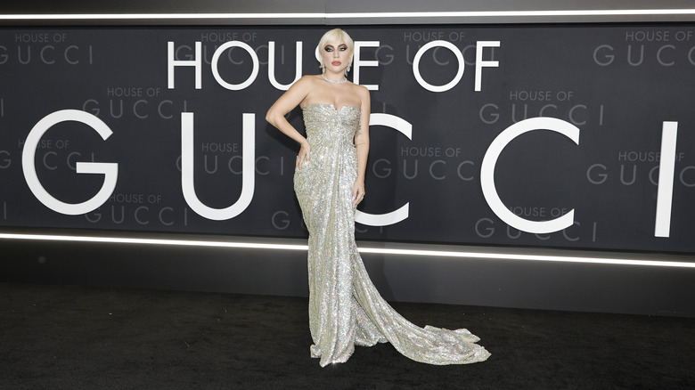 Lady Gaga posing in a silver strapless gown in front of a House of Gucci backdrop