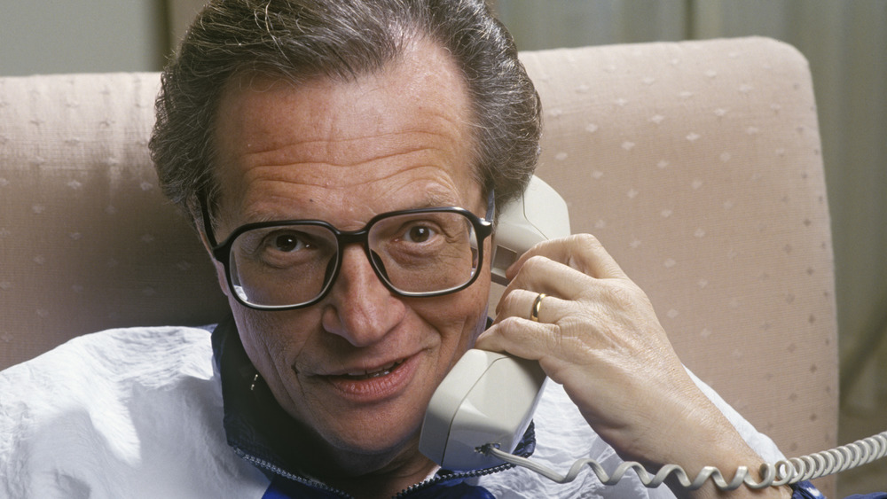 Larry King holding a phone while wearing black rimmed glasses